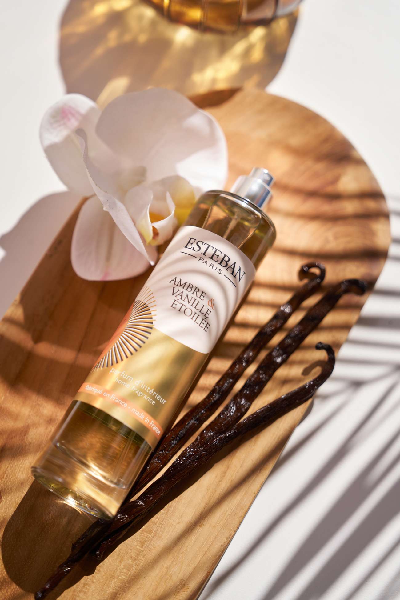 Parfum d’intérieur Esteban Paris Ambre & Vanille Étoilée en spray, flacon vaporisateur présenté avec des gousses de vanille et une orchidée blanche sur un support en bois